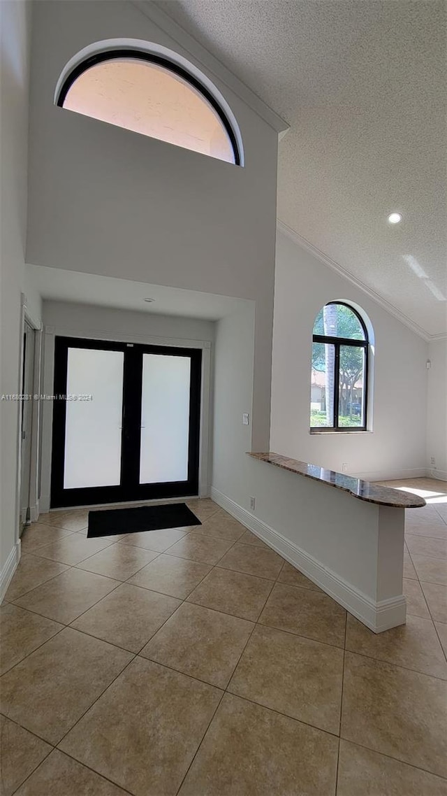 tiled empty room featuring ornamental molding, a textured ceiling, and high vaulted ceiling