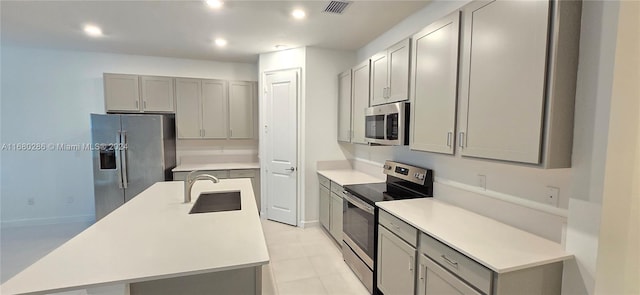 kitchen featuring gray cabinets, sink, an island with sink, and stainless steel appliances