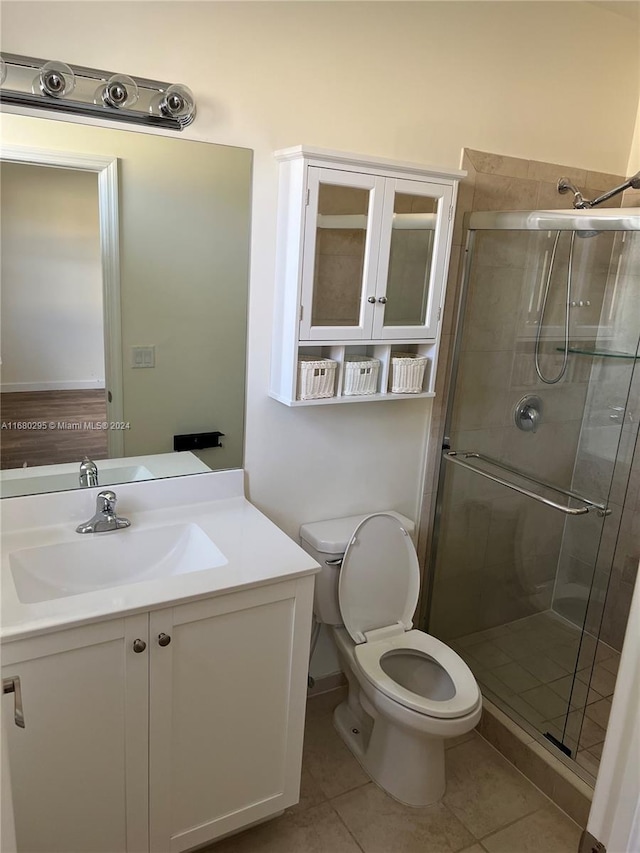 bathroom with tile patterned flooring, vanity, toilet, and a shower with door