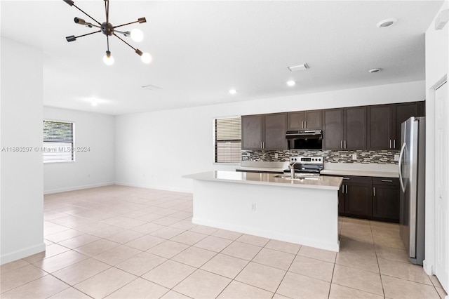 kitchen with appliances with stainless steel finishes, sink, a notable chandelier, light tile patterned floors, and a center island with sink