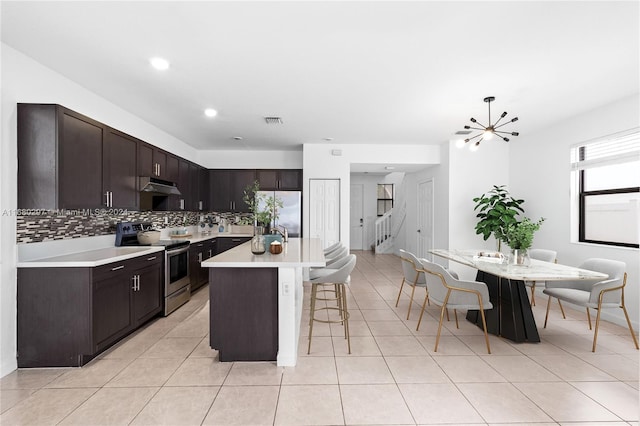 kitchen featuring decorative backsplash, a kitchen island, dark brown cabinets, a notable chandelier, and appliances with stainless steel finishes