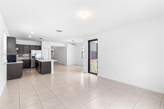 kitchen with an island with sink, backsplash, stainless steel fridge, light tile patterned floors, and a chandelier