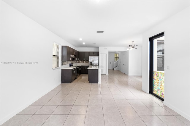 kitchen with light tile patterned flooring, backsplash, dark brown cabinets, stainless steel appliances, and a center island with sink