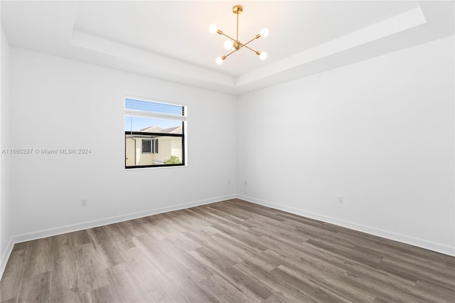 empty room with a notable chandelier, hardwood / wood-style floors, and a tray ceiling