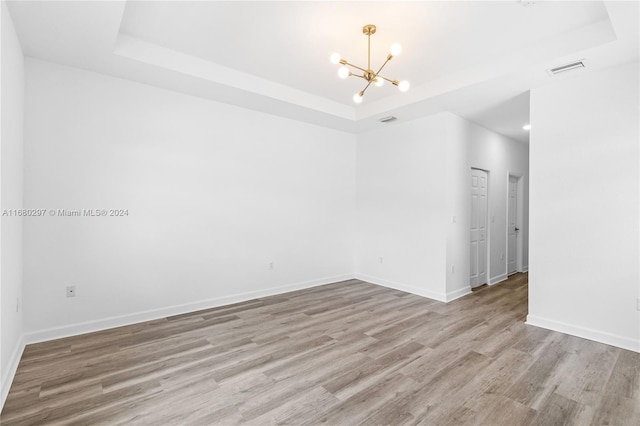 empty room featuring a raised ceiling, a chandelier, and light wood-type flooring