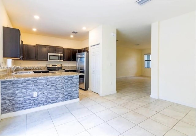 kitchen featuring kitchen peninsula, light stone countertops, sink, dark brown cabinetry, and stainless steel appliances