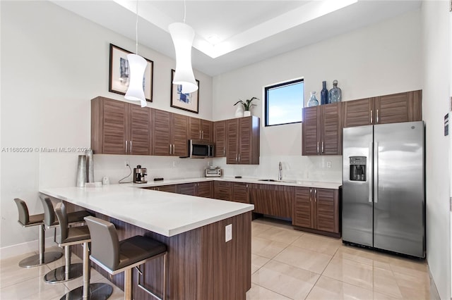 kitchen with appliances with stainless steel finishes, sink, light tile patterned flooring, a kitchen breakfast bar, and decorative light fixtures