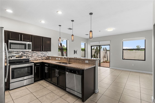 kitchen with kitchen peninsula, tasteful backsplash, hanging light fixtures, appliances with stainless steel finishes, and sink