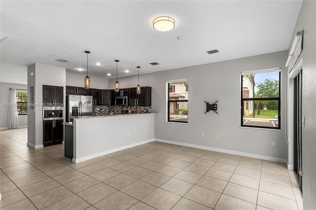 kitchen featuring dark brown cabinets, light tile patterned floors, backsplash, stainless steel appliances, and decorative light fixtures