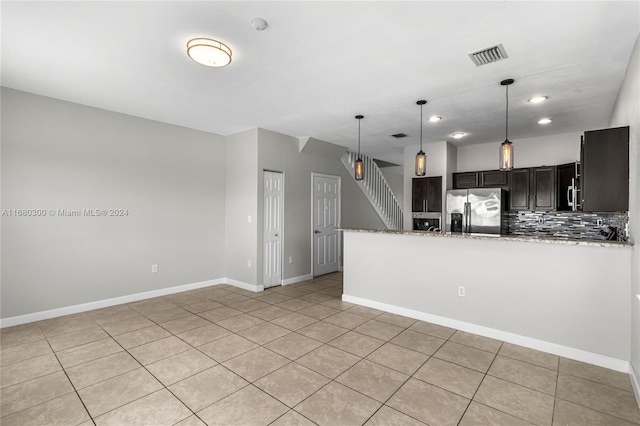 kitchen featuring light stone countertops, light tile patterned flooring, backsplash, stainless steel fridge, and decorative light fixtures