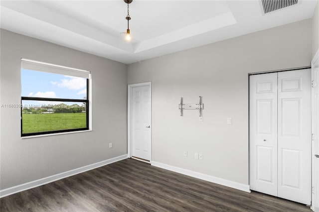 unfurnished bedroom featuring a closet, a raised ceiling, and dark hardwood / wood-style floors