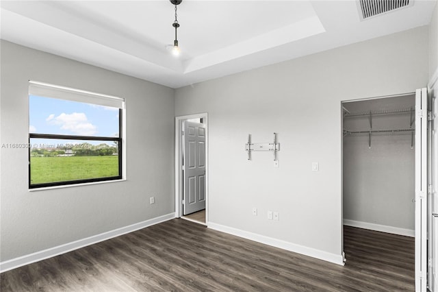 unfurnished bedroom with a closet, a raised ceiling, and dark hardwood / wood-style floors