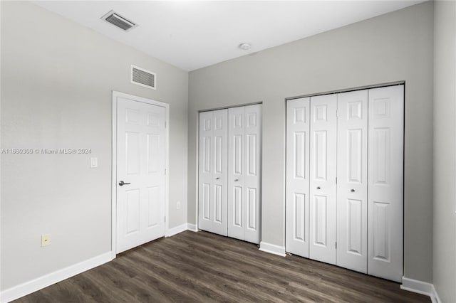 unfurnished bedroom featuring multiple closets and dark hardwood / wood-style flooring