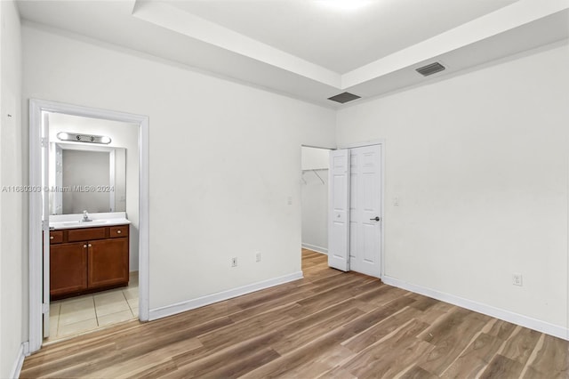 unfurnished bedroom with sink, ensuite bathroom, and hardwood / wood-style flooring