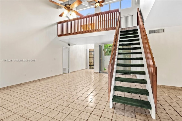 stairs with tile patterned flooring, ceiling fan, and a high ceiling