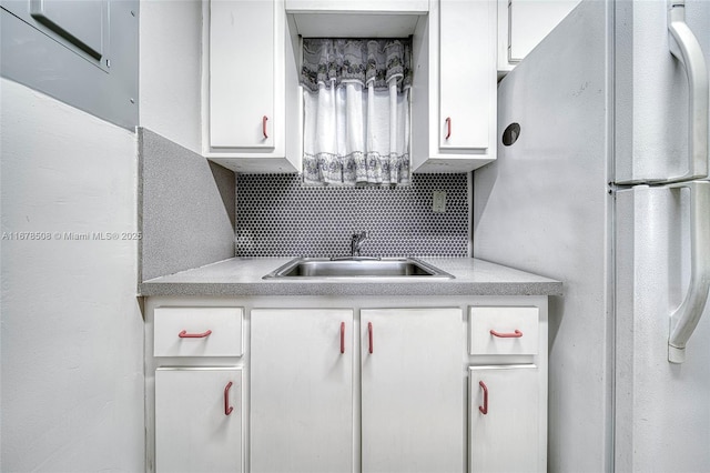 kitchen with white refrigerator, white cabinetry, backsplash, and sink