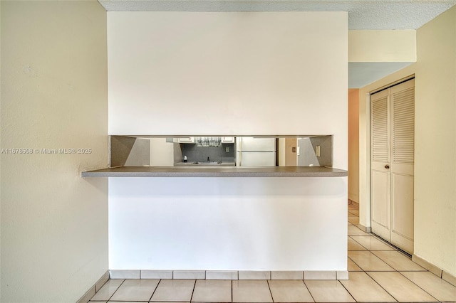 kitchen featuring white refrigerator, light tile patterned flooring, and kitchen peninsula