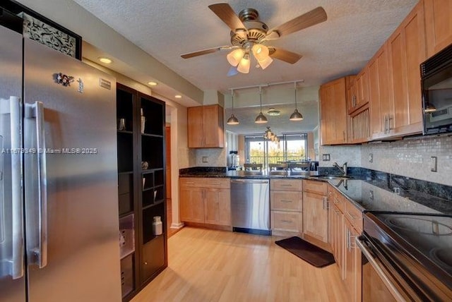 kitchen with black appliances, sink, dark stone countertops, light wood-type flooring, and decorative light fixtures