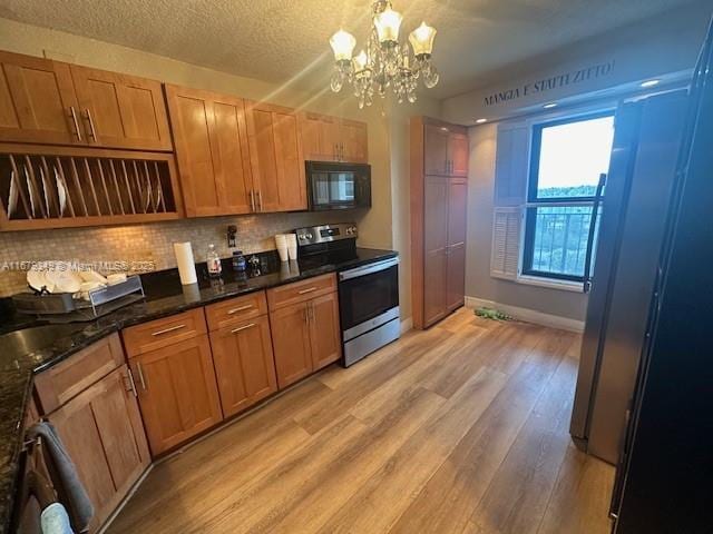 kitchen featuring pendant lighting, dark stone countertops, stainless steel range with electric cooktop, decorative backsplash, and light hardwood / wood-style flooring