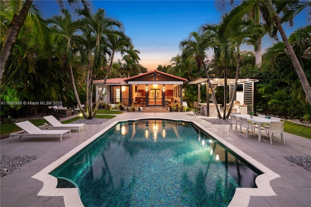 pool at dusk with a patio area, a bar, and an outbuilding