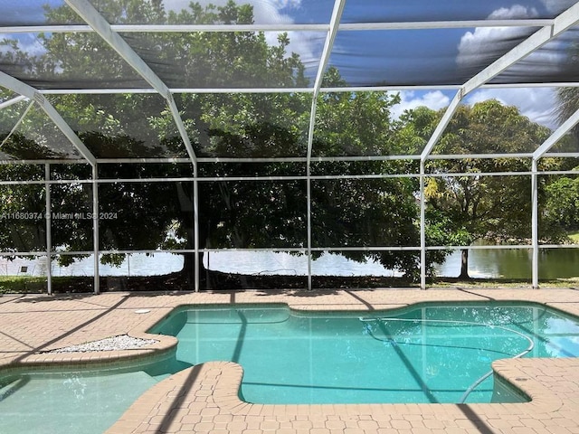 view of pool featuring a lanai, a water view, and a patio area