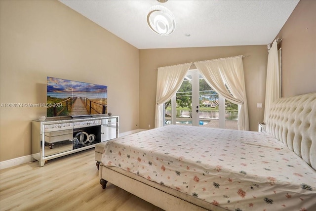 bedroom with access to exterior, a textured ceiling, hardwood / wood-style flooring, and vaulted ceiling