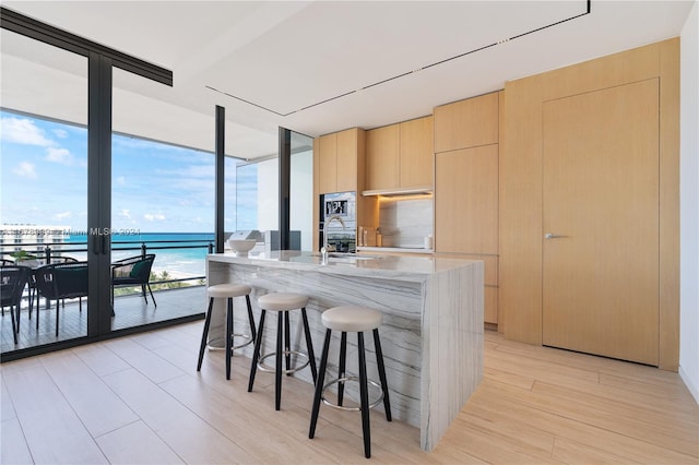 kitchen with a water view, light hardwood / wood-style floors, light brown cabinets, and a kitchen island with sink