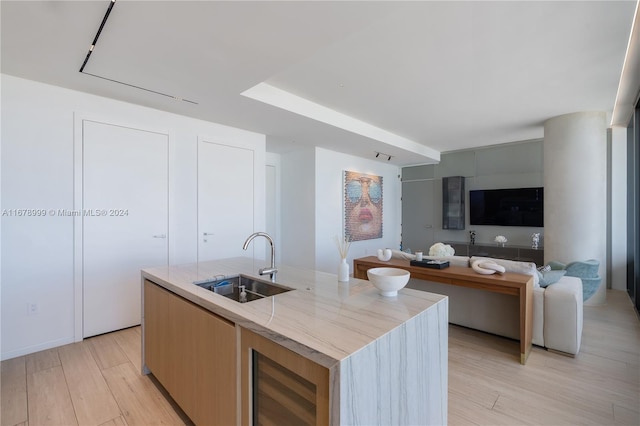 kitchen with a kitchen island with sink, light hardwood / wood-style flooring, sink, beverage cooler, and light brown cabinetry