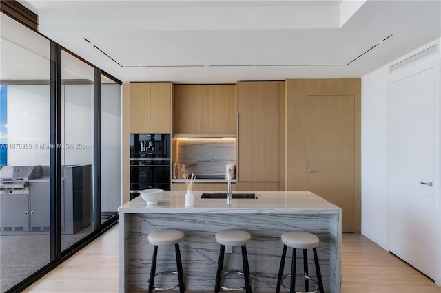 kitchen featuring light hardwood / wood-style floors, double oven, sink, and a kitchen bar