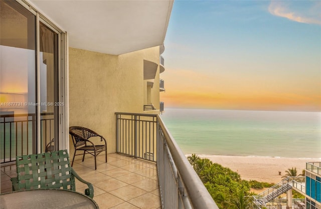 balcony at dusk featuring a water view and a view of the beach