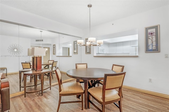 dining area with visible vents, light wood-style flooring, baseboards, and an inviting chandelier