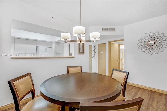 dining room featuring baseboards, wood finished floors, visible vents, and an inviting chandelier