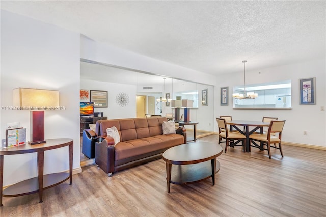 living room featuring a chandelier, a textured ceiling, baseboards, and wood finished floors