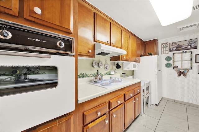 2451 Brickell Ave Unit 17G, Miami, FL 33129 - kitchen featuring under cabinet range hood, white appliances, brown cabinets, light countertops, and wallpapered walls