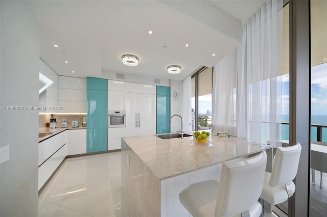 kitchen with white cabinetry, stainless steel oven, sink, and a center island with sink