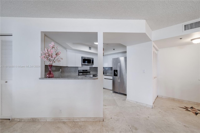 kitchen with stone counters, appliances with stainless steel finishes, a textured ceiling, white cabinetry, and decorative backsplash