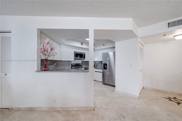 6767 Collins Ave Unit 602, Miami Beach, FL 33141 - kitchen with appliances with stainless steel finishes, white cabinetry, a peninsula, baseboards, and a tray ceiling