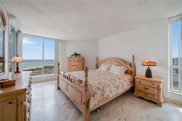 bedroom featuring expansive windows, multiple windows, a textured ceiling, and a water view