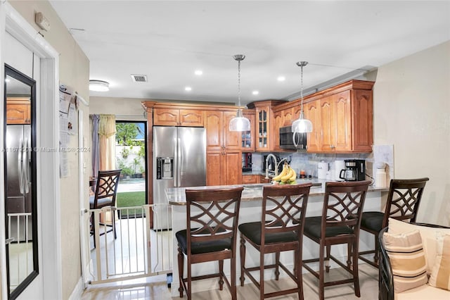 kitchen with appliances with stainless steel finishes, kitchen peninsula, hanging light fixtures, decorative backsplash, and a breakfast bar area