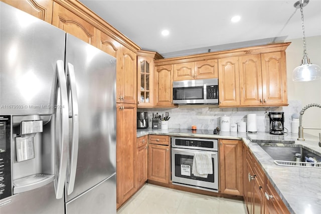 kitchen with backsplash, appliances with stainless steel finishes, light stone countertops, pendant lighting, and sink