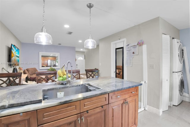 kitchen featuring sink, stacked washer and dryer, light stone counters, and pendant lighting