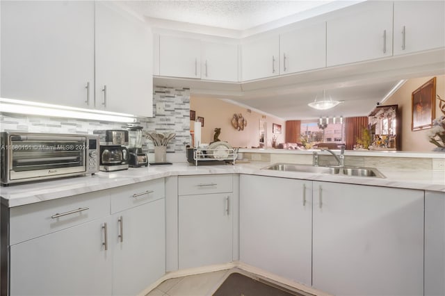 kitchen with white cabinetry, backsplash, a textured ceiling, and sink