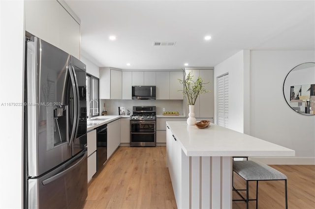 kitchen with light wood-type flooring, a center island, white cabinetry, stainless steel appliances, and a breakfast bar