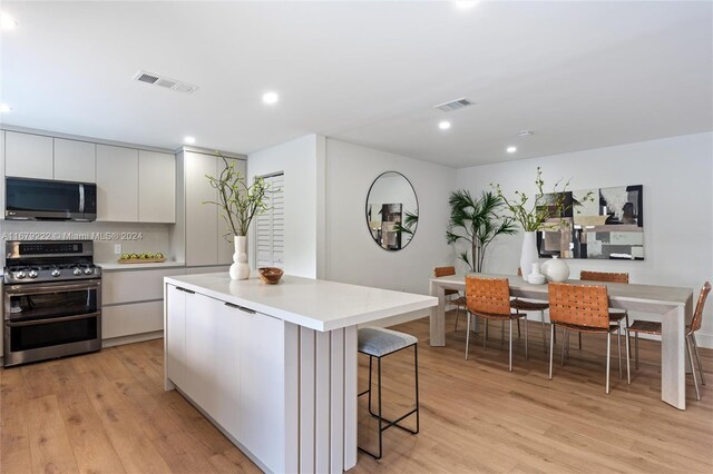 kitchen with stainless steel appliances, a center island, light wood-type flooring, white cabinetry, and tasteful backsplash