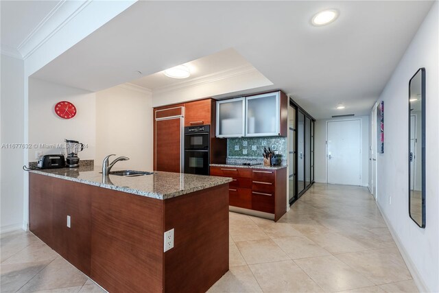 kitchen with stone countertops, kitchen peninsula, backsplash, sink, and black double oven