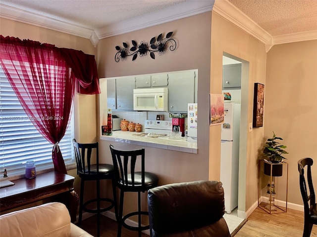 kitchen with white appliances, light wood-type flooring, a textured ceiling, tile counters, and ornamental molding