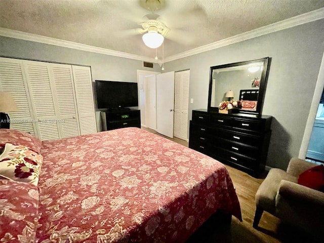 bedroom with ornamental molding, two closets, light wood-type flooring, and ceiling fan