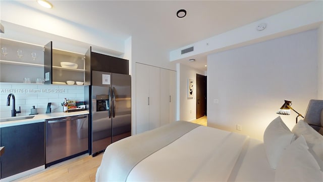 bedroom featuring a closet, light hardwood / wood-style flooring, stainless steel fridge with ice dispenser, and sink