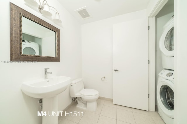 bathroom featuring stacked washing maching and dryer, sink, tile patterned flooring, and toilet