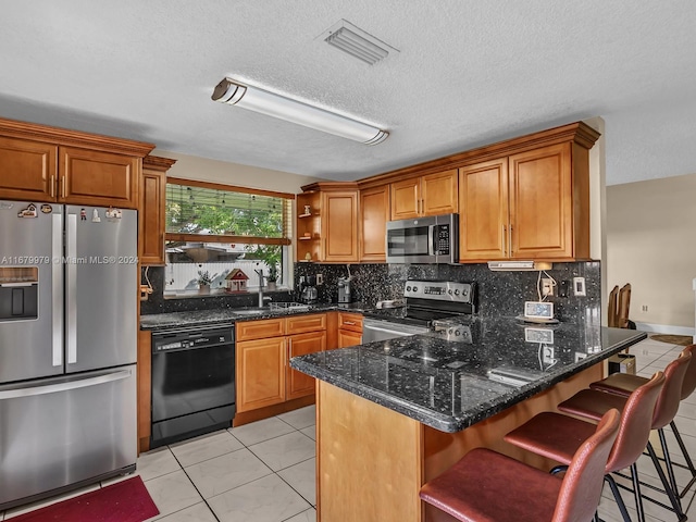 kitchen with stainless steel appliances, dark stone countertops, sink, a breakfast bar, and light tile patterned floors